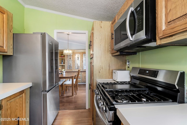 kitchen featuring wood finished floors, stainless steel appliances, a textured ceiling, crown molding, and a chandelier