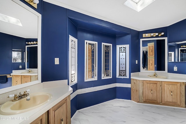 bathroom with marble finish floor, a skylight, two vanities, and a sink