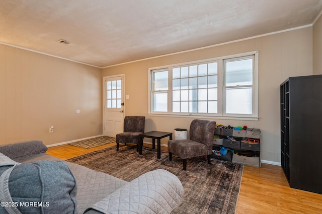 living room featuring light wood-style flooring, baseboards, visible vents, and ornamental molding