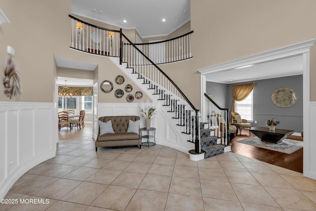 staircase with tile patterned floors, crown molding, a wainscoted wall, and a chandelier