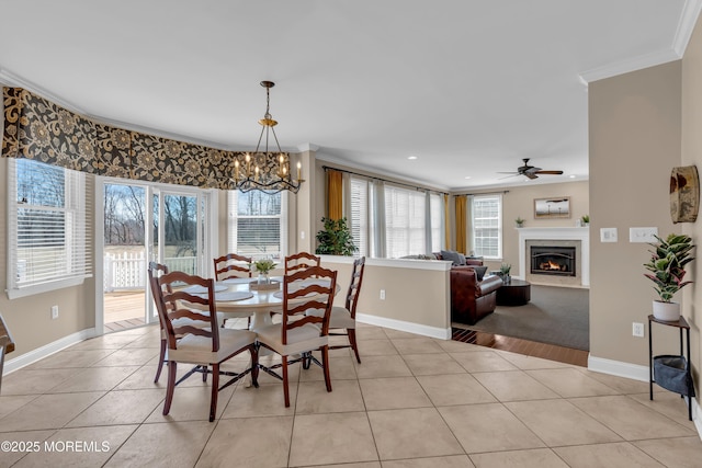 dining room featuring ceiling fan with notable chandelier, a glass covered fireplace, light tile patterned flooring, crown molding, and baseboards