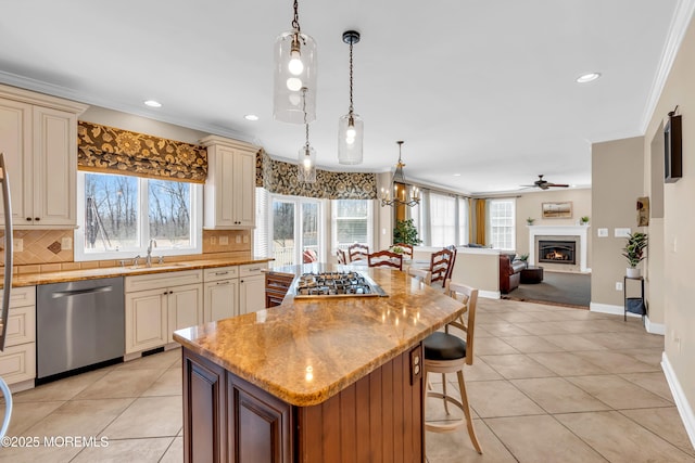 kitchen with ceiling fan with notable chandelier, appliances with stainless steel finishes, cream cabinets, light tile patterned flooring, and a sink