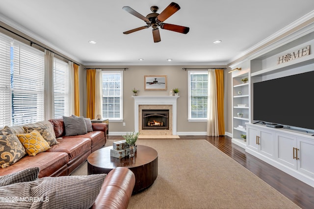 living area featuring built in shelves, dark wood-type flooring, ceiling fan, crown molding, and a fireplace