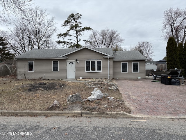 single story home with decorative driveway, roof with shingles, and fence