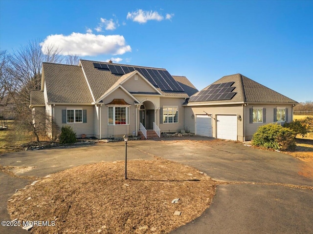 view of front facade featuring roof with shingles, solar panels, entry steps, concrete driveway, and a garage