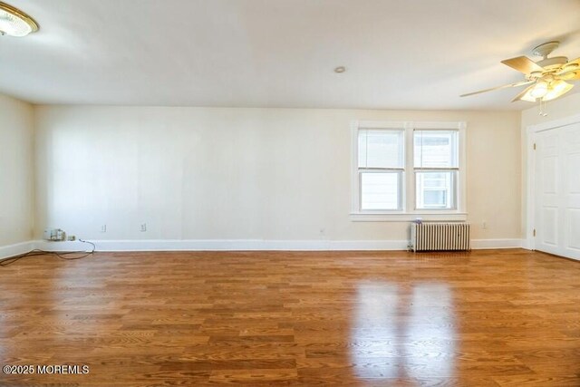 spare room with wood finished floors, a ceiling fan, baseboards, and radiator