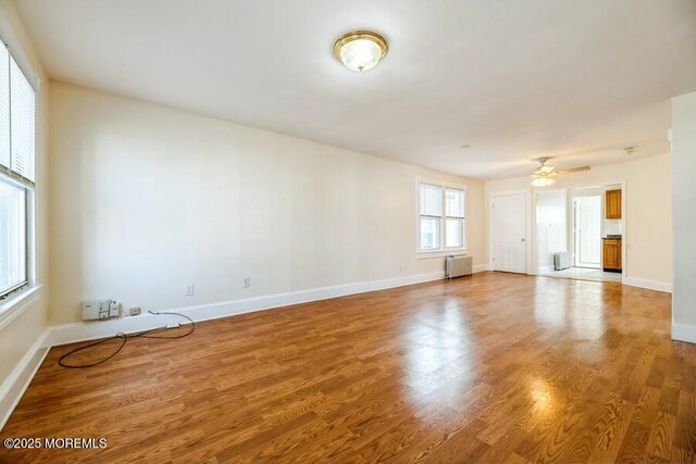 spare room with radiator heating unit, wood finished floors, a ceiling fan, and baseboards
