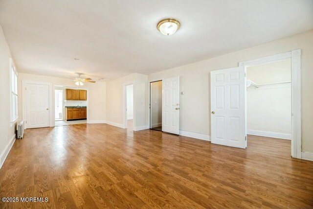 unfurnished living room featuring baseboards, radiator heating unit, wood finished floors, and a ceiling fan