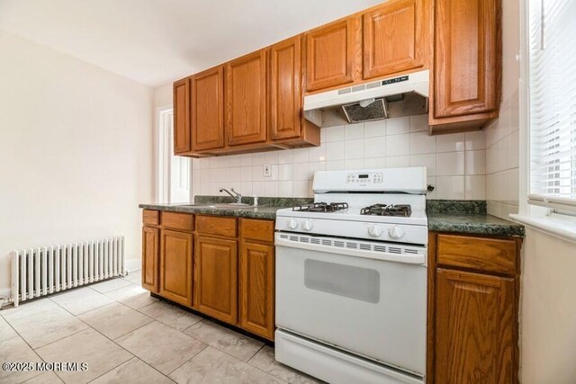 kitchen featuring a sink, under cabinet range hood, white range with gas stovetop, radiator heating unit, and dark countertops