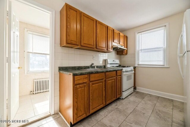 kitchen with brown cabinets, dark countertops, under cabinet range hood, radiator heating unit, and white appliances