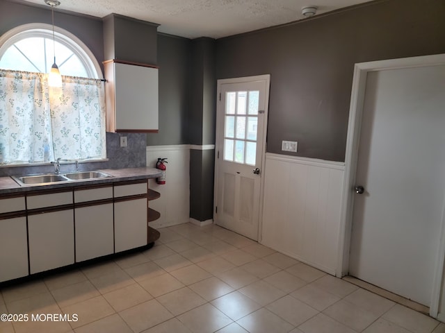 kitchen featuring white cabinets, pendant lighting, a wainscoted wall, and a sink