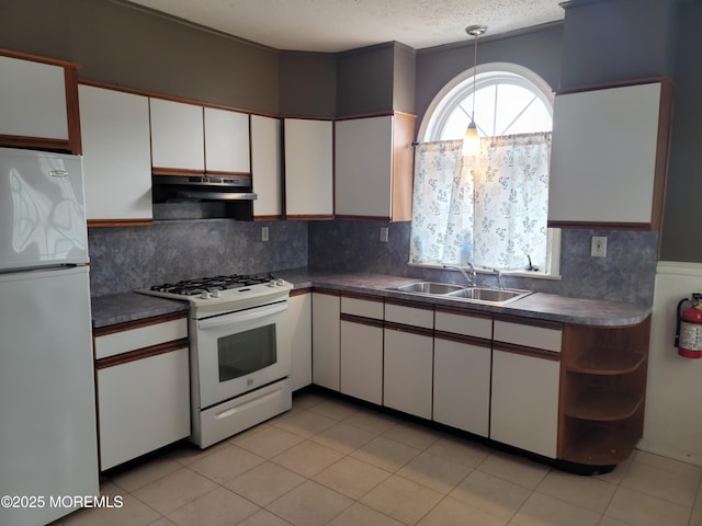 kitchen with white cabinetry, a sink, dark countertops, under cabinet range hood, and white appliances