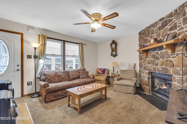 living area with a stone fireplace, a ceiling fan, and carpet floors