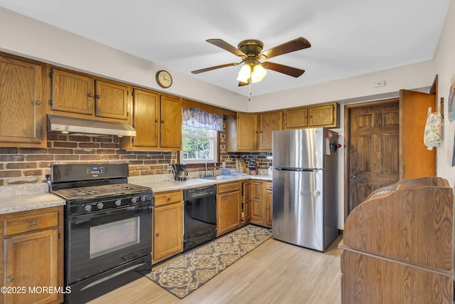 kitchen with brown cabinets, black appliances, under cabinet range hood, a sink, and light countertops