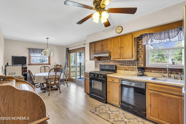 kitchen featuring a sink, black appliances, light countertops, under cabinet range hood, and tasteful backsplash