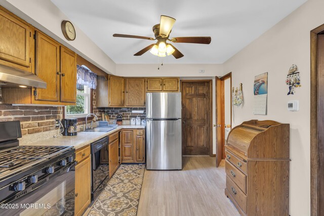 kitchen featuring tasteful backsplash, light countertops, brown cabinets, black appliances, and a sink