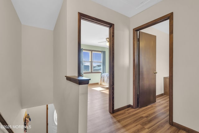 hall with an upstairs landing, baseboards, and wood finished floors