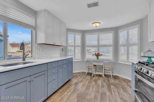 kitchen featuring visible vents, range with two ovens, light wood-style floors, and a sink