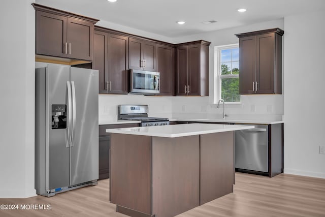 kitchen with stainless steel appliances, dark brown cabinetry, a center island, and light countertops