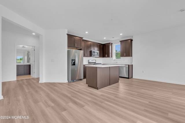 kitchen with light wood-style flooring, stainless steel appliances, dark brown cabinetry, light countertops, and a center island