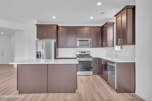 kitchen with a kitchen island, light wood-style flooring, a sink, stainless steel appliances, and dark brown cabinets