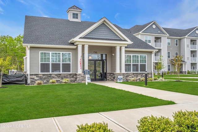 view of front of house with stone siding, french doors, a shingled roof, and a front yard