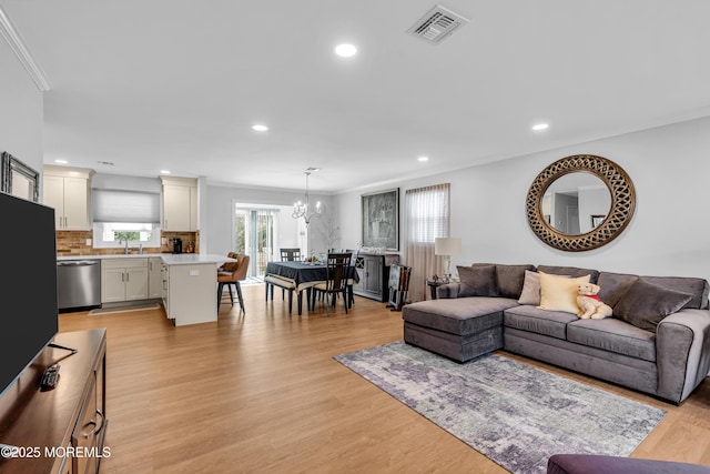 living area featuring visible vents, light wood-style floors, crown molding, and a notable chandelier