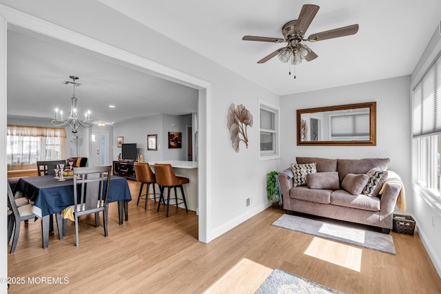 living area with ceiling fan with notable chandelier, light wood-style floors, and baseboards