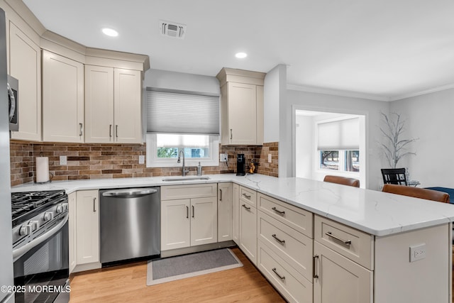 kitchen with visible vents, a peninsula, a sink, appliances with stainless steel finishes, and light wood-type flooring