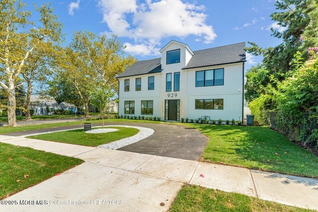 view of front of home featuring stucco siding, curved driveway, a front yard, and fence