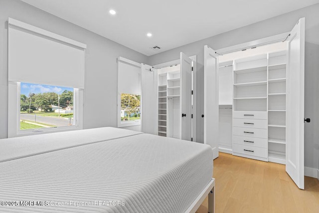 bedroom featuring a walk in closet, light wood-style flooring, recessed lighting, and visible vents