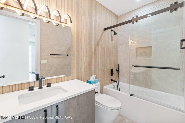 bathroom featuring vanity, toilet, tile walls, and bath / shower combo with glass door