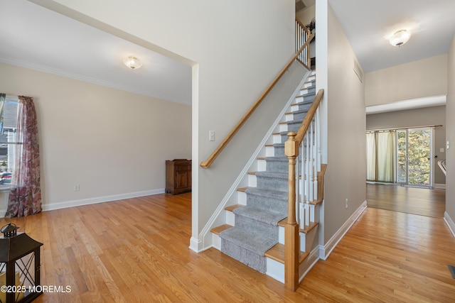 stairs featuring wood finished floors, baseboards, and ornamental molding