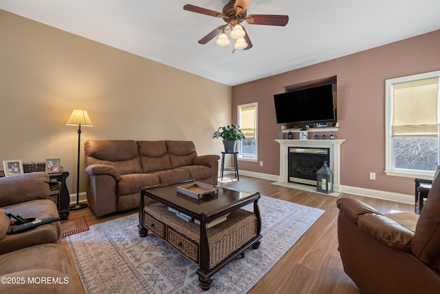 living area featuring ceiling fan, baseboards, wood finished floors, and a fireplace with flush hearth