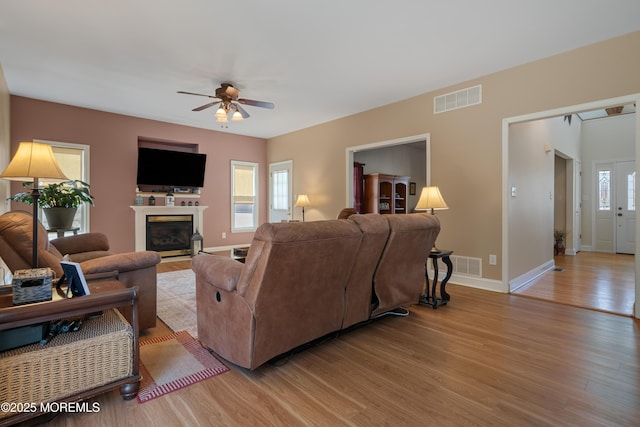 living room with a glass covered fireplace, light wood-style flooring, a ceiling fan, and visible vents