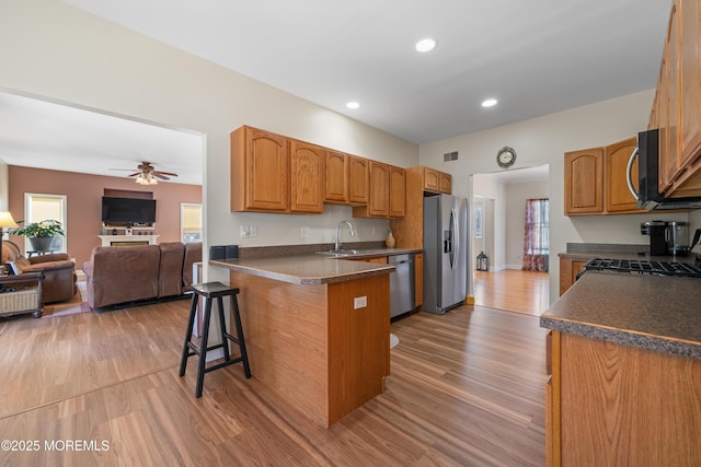 kitchen featuring dark countertops, a peninsula, light wood-type flooring, and appliances with stainless steel finishes