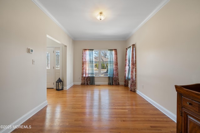 spare room featuring crown molding, light wood-type flooring, and baseboards