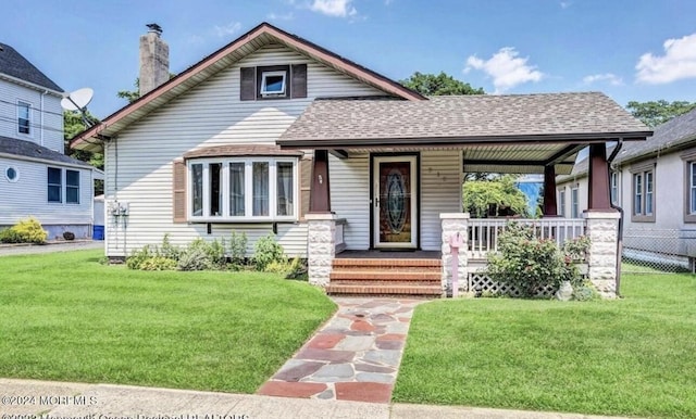 view of front of house with a chimney, roof with shingles, a porch, and a front yard