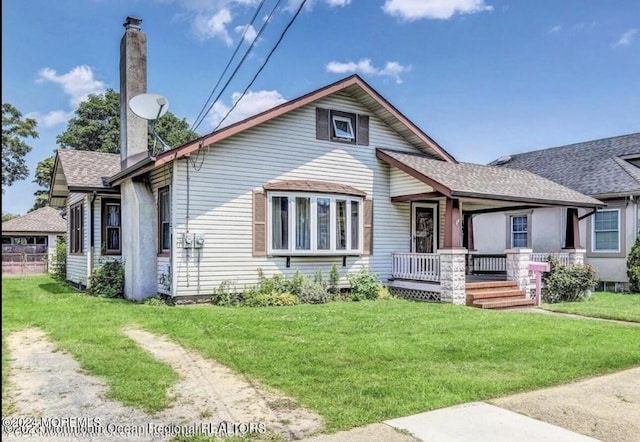 view of front of home with a porch, a chimney, a front yard, and a shingled roof