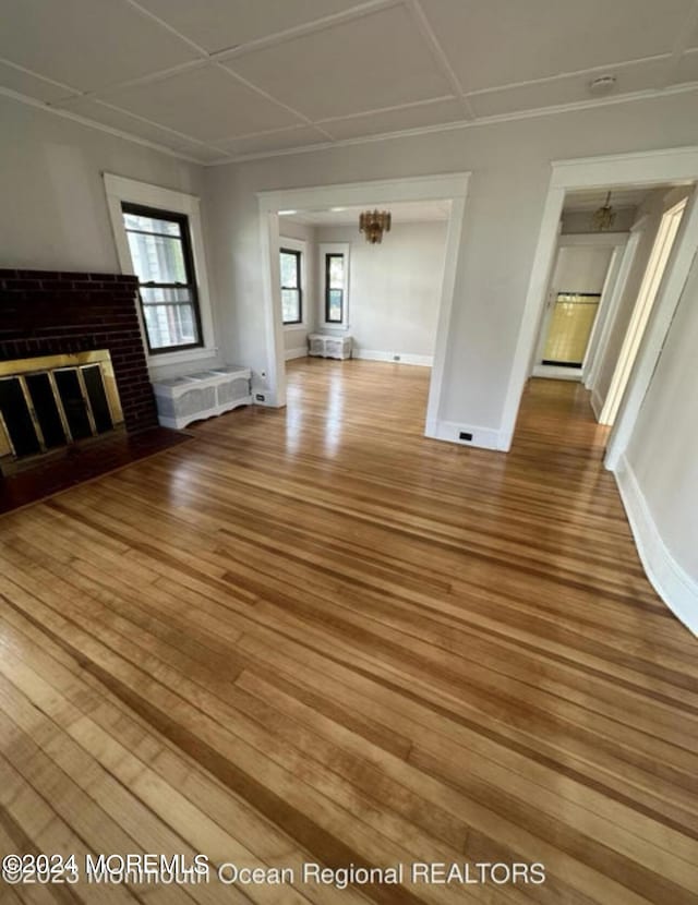 unfurnished living room featuring wood finished floors, radiator heating unit, baseboards, a brick fireplace, and a chandelier