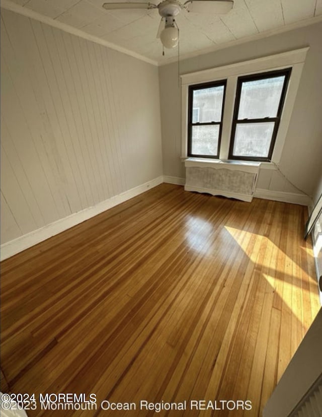 spare room featuring ceiling fan, baseboards, wood finished floors, and ornamental molding