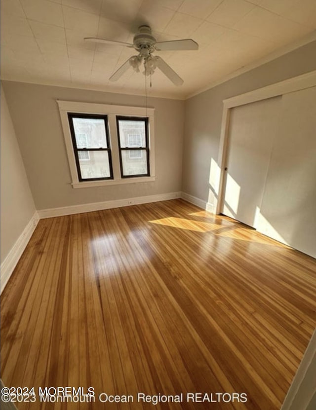 spare room featuring crown molding, baseboards, wood-type flooring, and ceiling fan