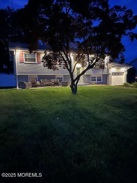 back of house at twilight featuring a lawn and a garage