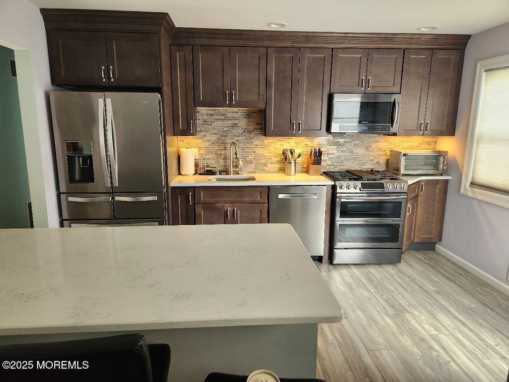 kitchen with decorative backsplash, light wood-style flooring, stainless steel appliances, and a sink