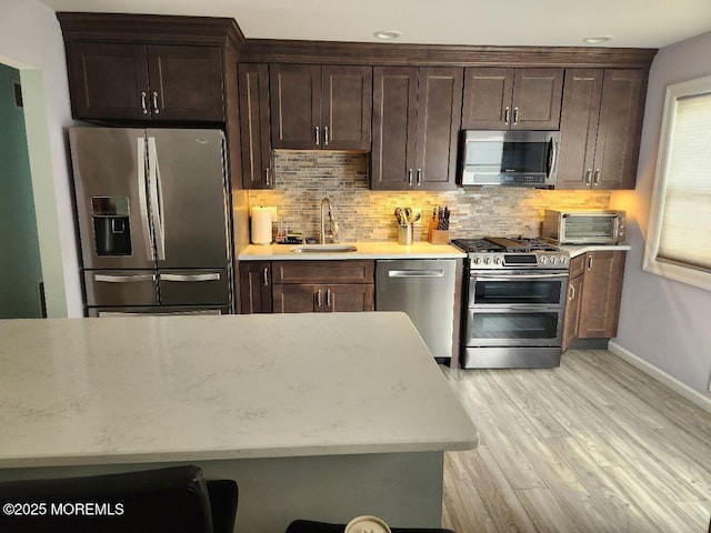 kitchen with decorative backsplash, light wood-style flooring, stainless steel appliances, and a sink