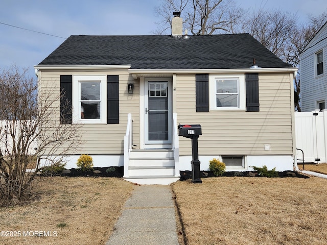 bungalow-style home with a front lawn, fence, a chimney, and a shingled roof