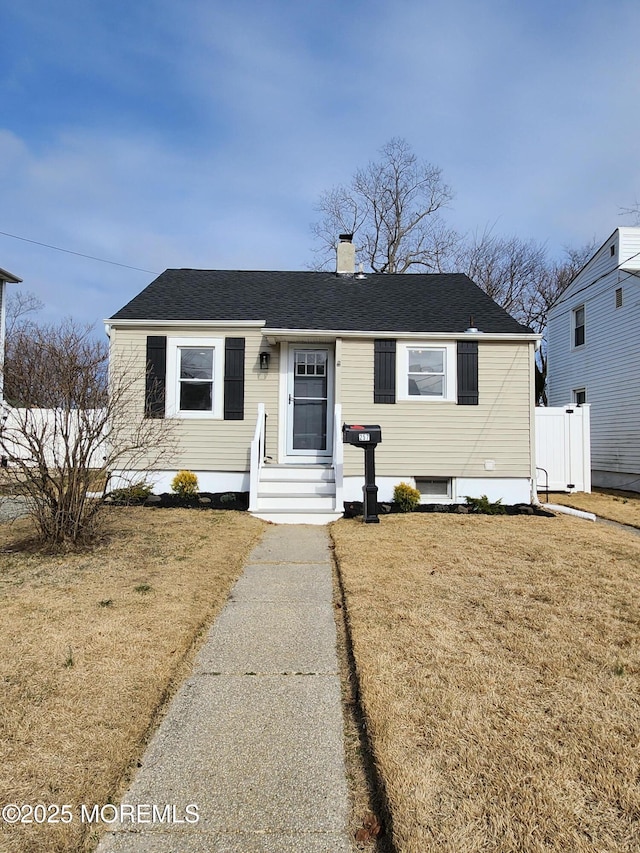 view of front of property featuring a chimney, a front lawn, and a shingled roof