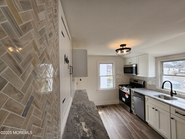 kitchen with light stone counters, a sink, stainless steel appliances, white cabinets, and tasteful backsplash