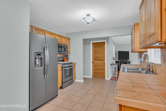 kitchen featuring tile countertops, light tile patterned flooring, a sink, stainless steel refrigerator with ice dispenser, and gas range