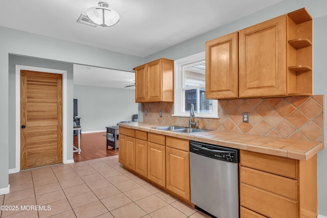 kitchen featuring a sink, stainless steel dishwasher, light tile patterned floors, decorative backsplash, and tile counters